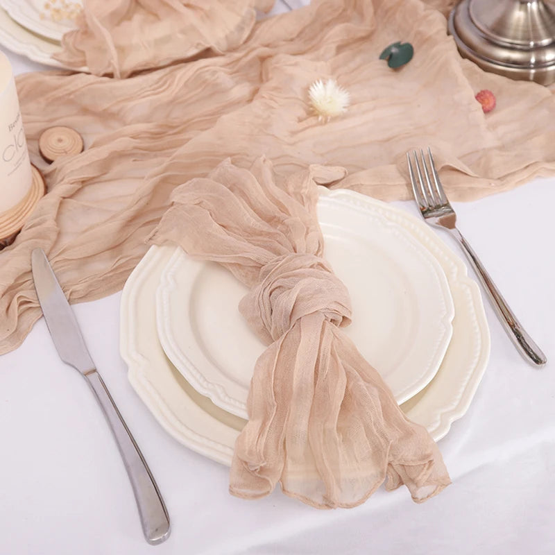 Assiette blanche avec serviette beige chiffonnée sur une table, couverts en métal posés à côté.