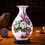 Un vase en porcelaine blanche décoré de fleurs de pivoines et de prunus en fleurs, ainsi que d'un oiseau, sur un socle en bois foncé.