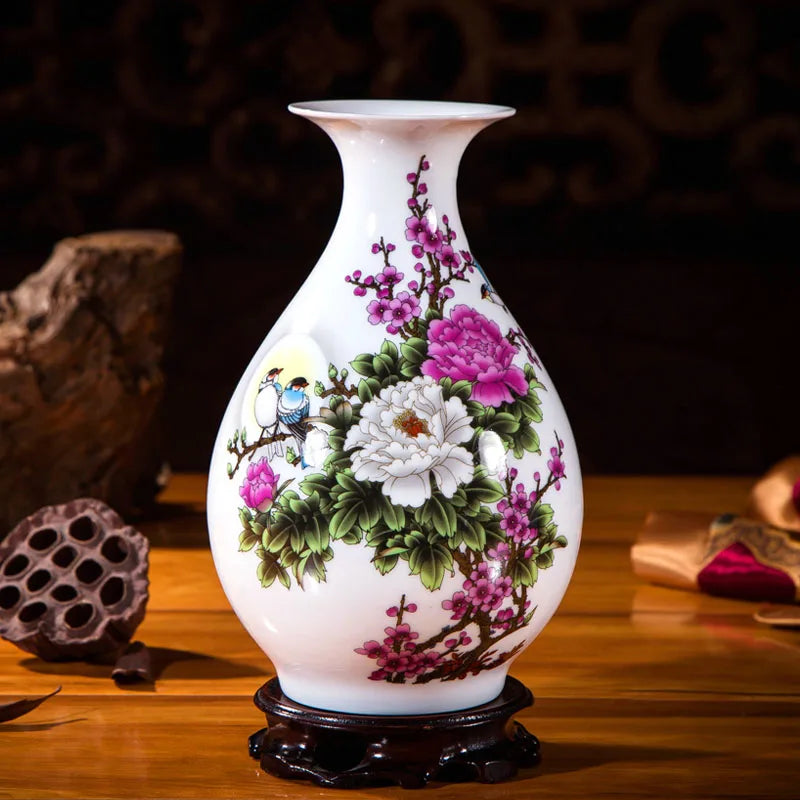 Vase en porcelaine blanche orné de fleurs rose et de motifs floraux délicats avec un oiseau en vol, posé sur un socle en bois foncé.