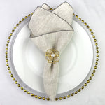Serviette de table grise avec ornement floral doré sur un plateau décoratif avec des perles dorées.