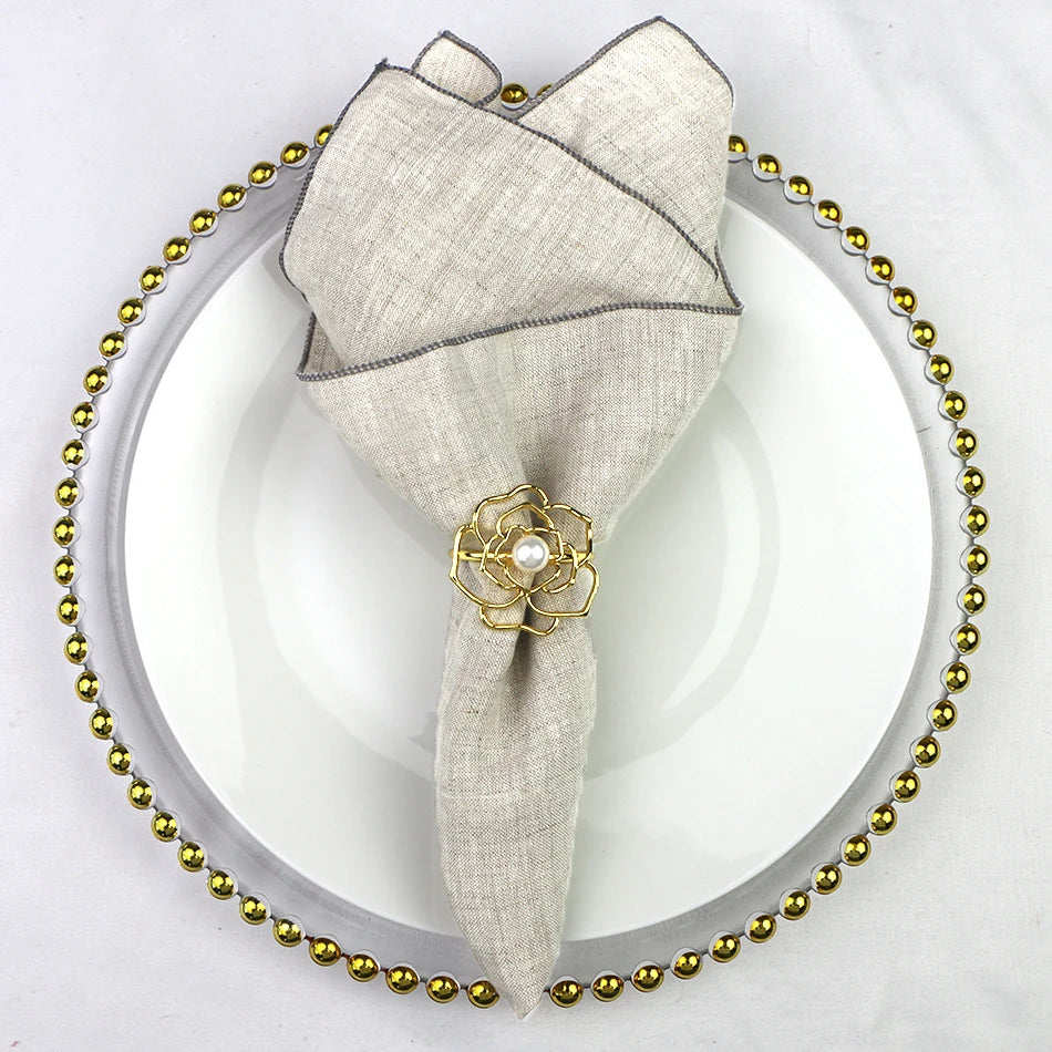 Serviette de table grise avec ornement floral doré sur un plateau décoratif avec des perles dorées.