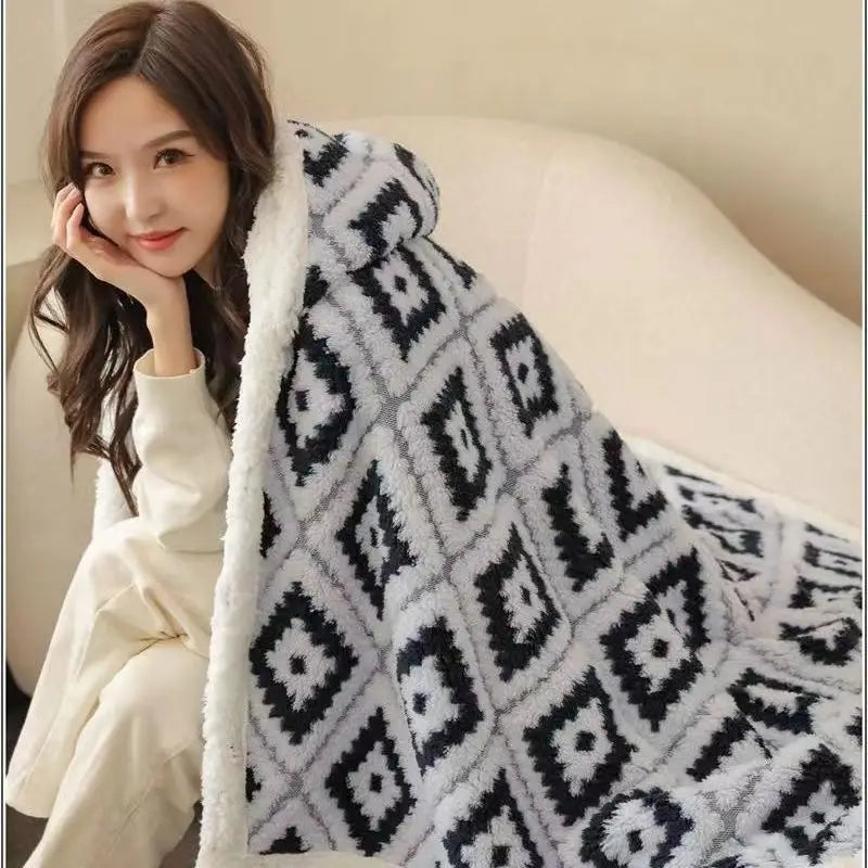 Une jeune femme souriante, habillée d'un pull blanc, enveloppée dans une couverture grise et blanche à motifs géométriques, profite d'un moment de détente et de confort.