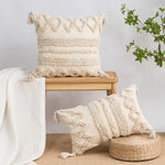 Coussin décoratif en tissu doux et moelleux avec des motifs texturés et des franges, placé sur un banc en bois, entouré de plantes vertes dans une atmosphère naturelle et apaisante.