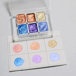 peintures aquarelle palette compacte bleu vert violet rose beige jaune blanc texture granuleuse opaques