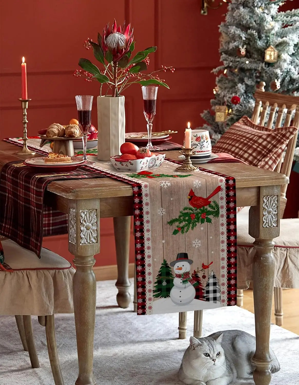 Décor de table de Noël festif avec centre de table orné de fleurs tropicales, verres à vin, et présence d'un chat gris au premier plan.