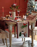 Décor de table de Noël festif avec centre de table orné de fleurs tropicales, verres à vin, et présence d'un chat gris au premier plan.