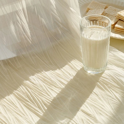 Verre de lait sur une table recouverte du voilage blanc froissé laissant passer la lumière du matin.