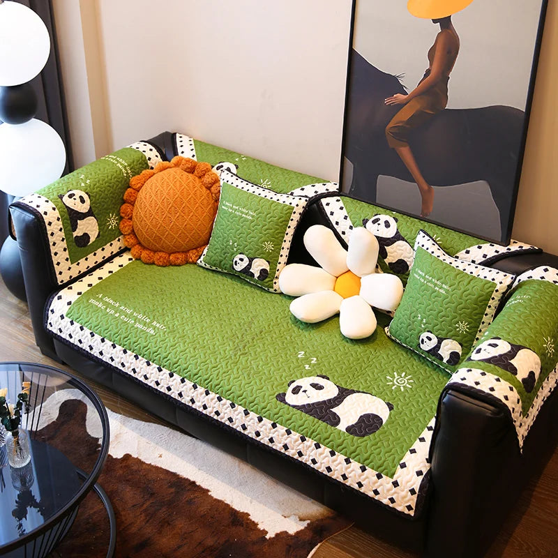 Coussin décoratif avec motifs de pandas et de fleurs sur canapé vert dans un intérieur moderne.