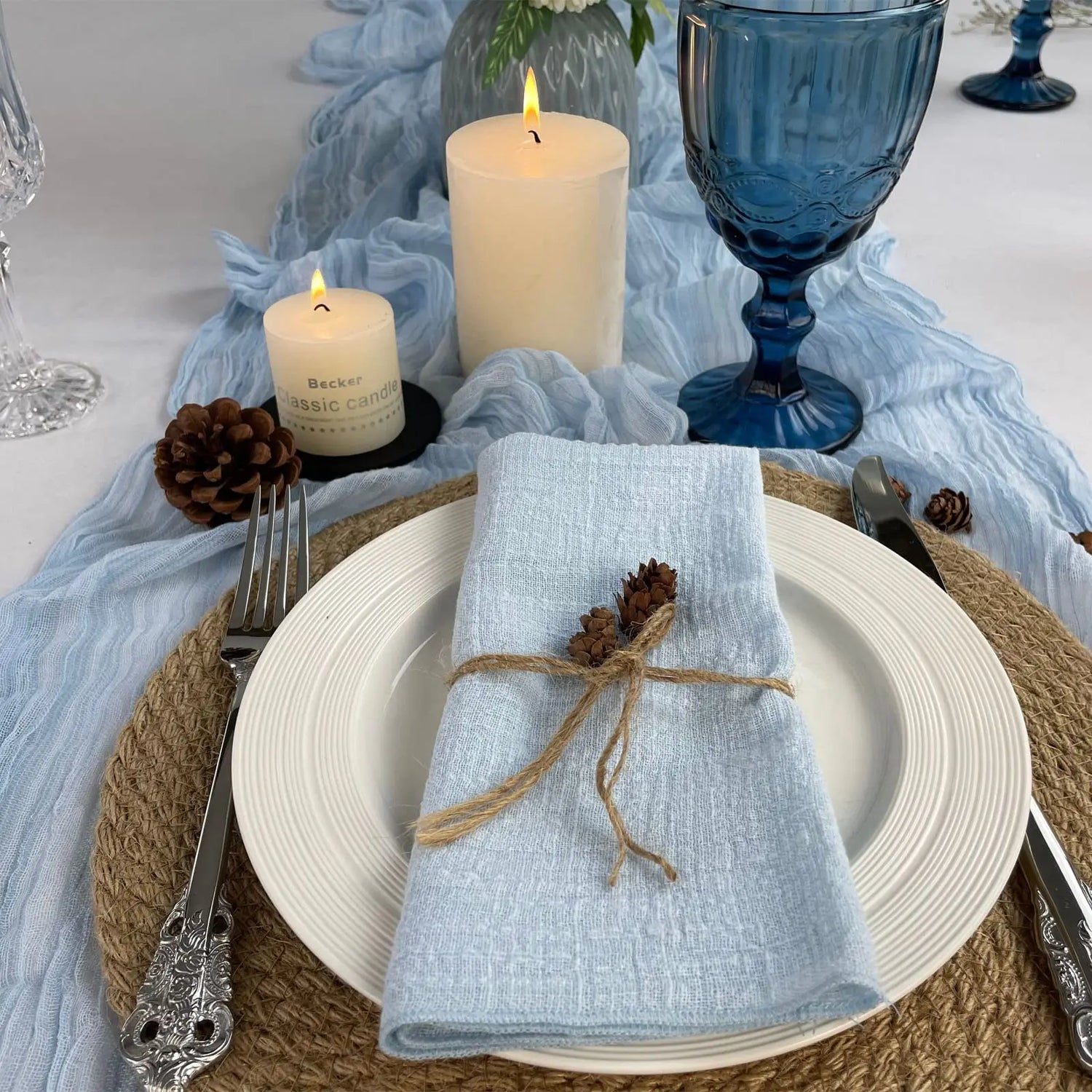 Une table dressée avec élégance, ornée de bougies allumées, de verres en cristal bleu et de décorations en fibres naturelles, créant une atmosphère chaleureuse et apaisante.