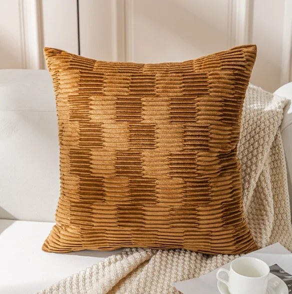 Coussin décoratif en velours côtelé de couleur ocre sur un canapé blanc, accompagné d'une couverture en tricot.