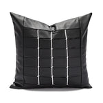 Coussin décoratif noir en cuir avec motif géométrique en blanc.