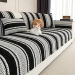 Un chat blanc pelucheux est allongé sur un lit avec une couverture à rayures noires et blanches.