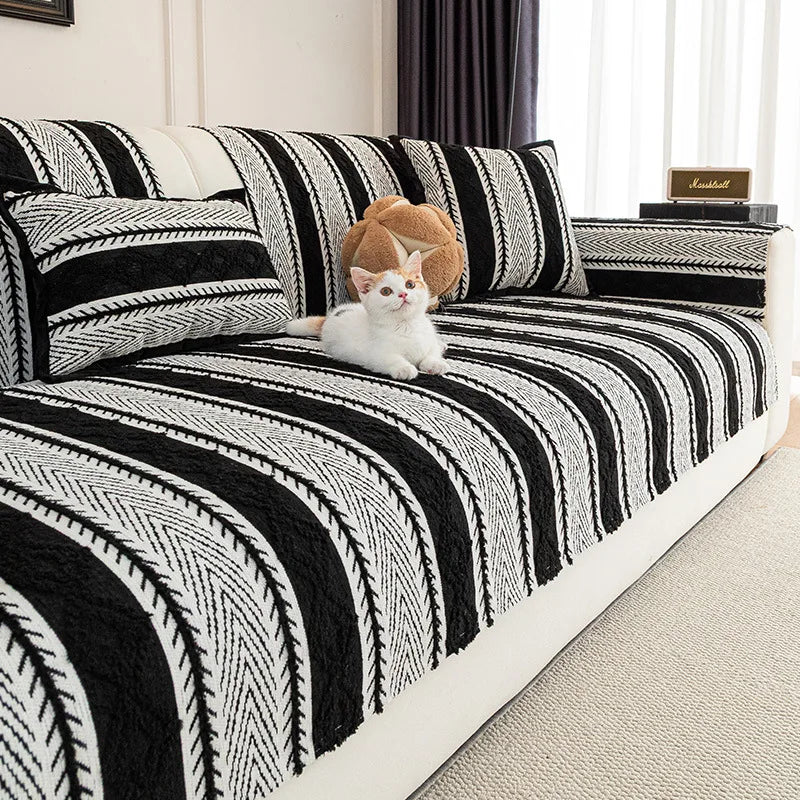 Un chat blanc pelucheux est allongé sur un lit avec une couverture à rayures noires et blanches.