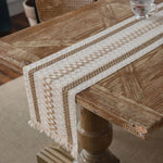 Cette image montre une table en bois avec un chemin de table tissé en couleurs beige et blanches, créant un motif décoratif intéressant sur la surface de la table.