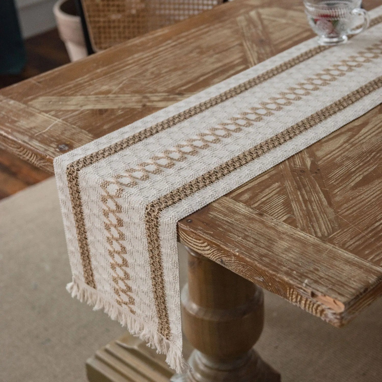 Cette image montre une table en bois avec un chemin de table tissé en couleurs beige et blanches, créant un motif décoratif intéressant sur la surface de la table.