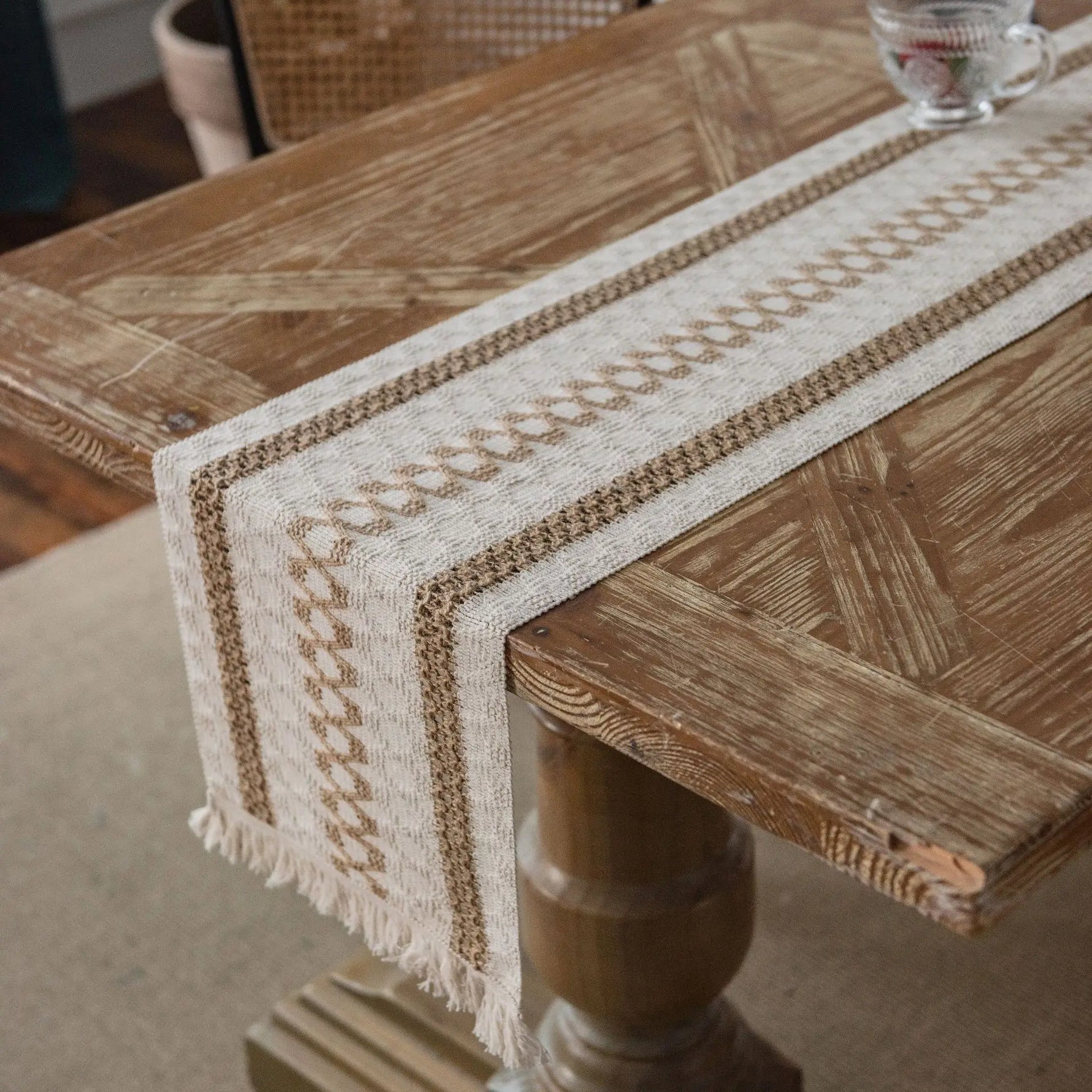 Cette image montre une table en bois avec un chemin de table tissé en couleurs beige et blanches, créant un motif décoratif intéressant sur la surface de la table.