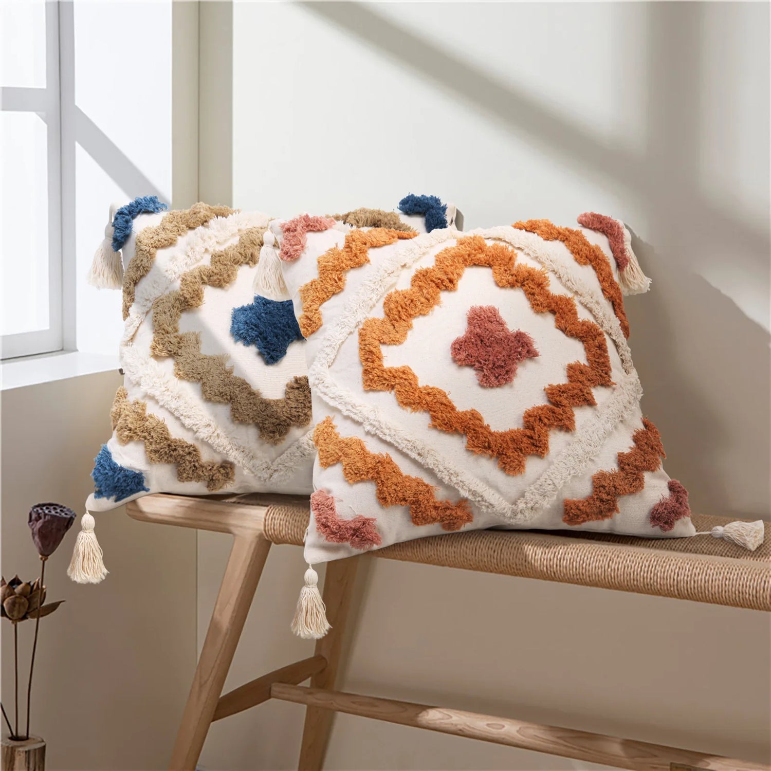 Coussin décoratif avec motif géométrique coloré et franges, placé sur un banc en bois dans un intérieur lumineux.