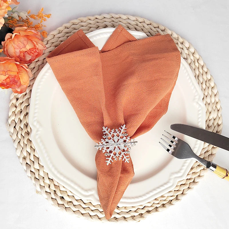 Un joli arrangement de table d'automne avec une assiette blanche, des serviettes en tissu orange et une décoration de flocon de neige en métal sur un napperon tressé.