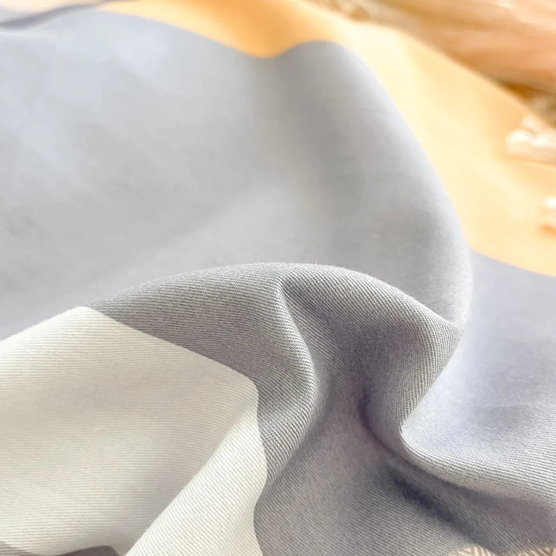 Gros plan sur un tissu gris plissé avec des reflets de lumière dorée, créant une texture et une douceur visuelle.