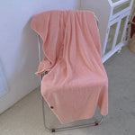 Une couverture douillette et confortable de couleur rose saumon posée sur un fauteuil.