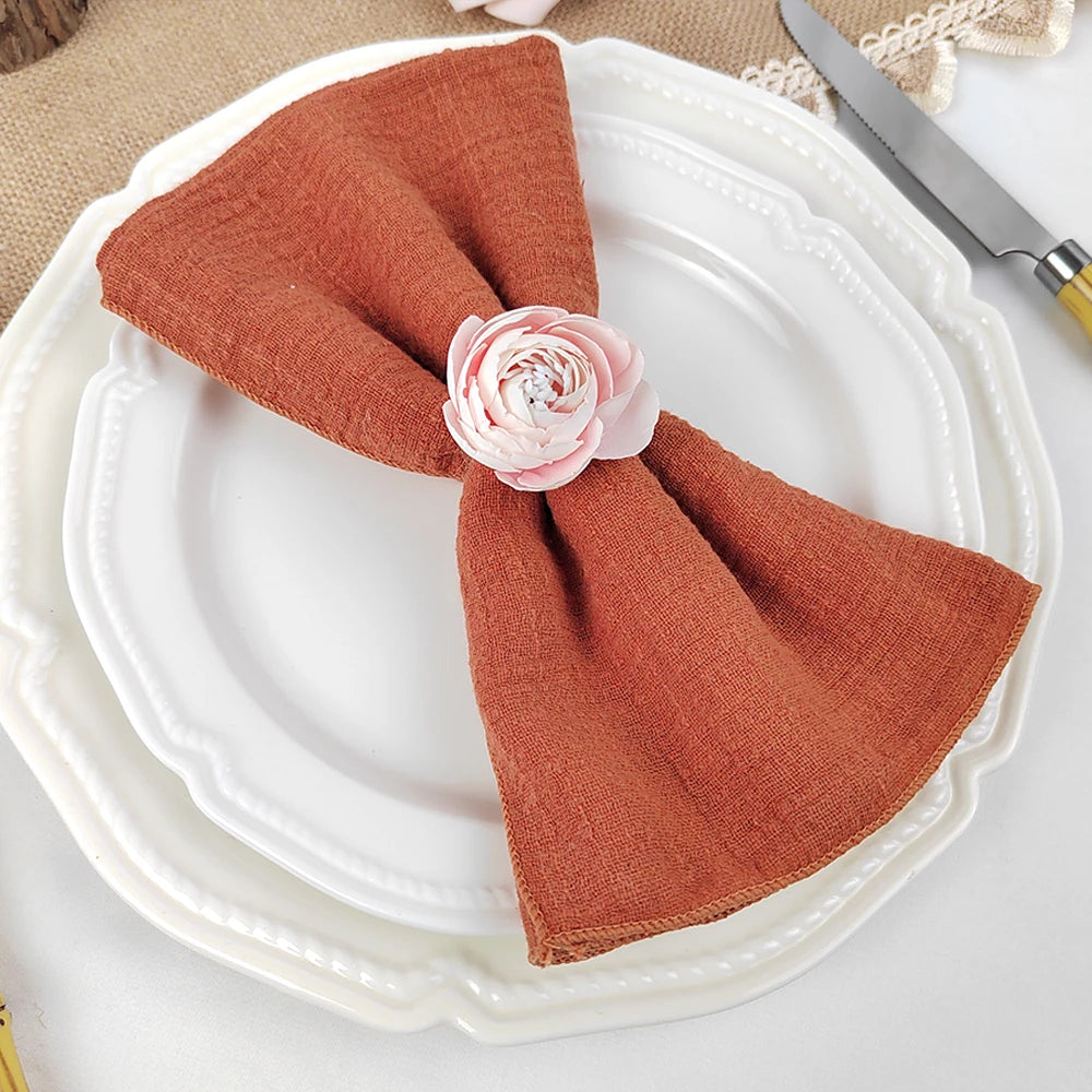 Une serviette en tissu orange vif attachée avec une délicate fleur rose sur une assiette blanche vintage.