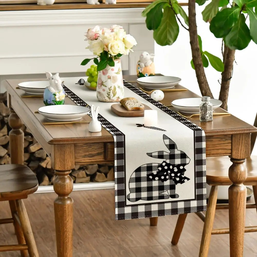 Une élégante décoration de table avec un chemin de table orné d'un motif de lapin à carreaux noirs et blancs, accompagnée de bouquets de fleurs et d'accessoires décoratifs, créant une ambiance chaleureuse et printanière.