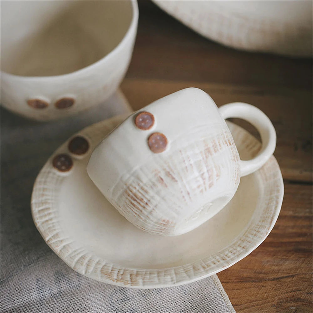 Deux tasses de thé en céramique blanche décorées de motifs géométriques et de points rouges, posées sur une table en bois.