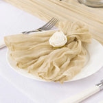 Une élégante serviette de table beige, ornée d'une rose blanche, est posée sur une assiette blanche avec des couverts.
