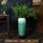 Un magnifique vase vert foncé décoré de végétation luxuriante, créant une ambiance naturelle et apaisante dans un intérieur rustique.