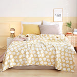 Couverture de lit jaune et blanche à pois avec de nombreux oreillers moelleux sur un lit confortable dans une chambre chaleureuse et accueillante.