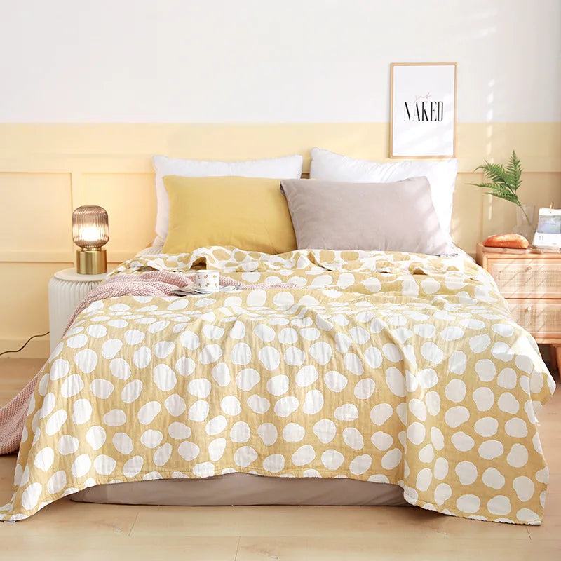 Couverture de lit jaune et blanche à pois avec de nombreux oreillers moelleux sur un lit confortable dans une chambre chaleureuse et accueillante.