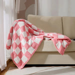 Une belle couverture en coton rose pâle et blanc, disposée de manière élégante sur un canapé beige, créant une ambiance chaleureuse et confortable dans cette pièce.