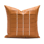 Coussin carré en cuir marron avec motif géométrique en surpiqûres blanches, donnant un style moderne et épuré.