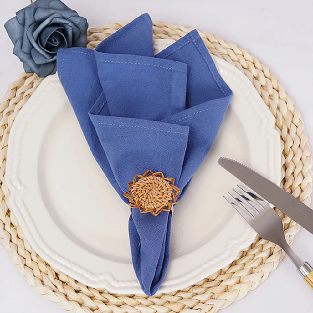 Sur une assiette blanche repose un arrangement de serviettes de table bleues pliées, ornées d'un motif floral en bois. Une fourchette et un couteau sont disposés à côté.