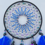 Attrape-rêves rond avec motifs géométriques bleus et violets, décoré de perles multicolores et de plumes bleues.