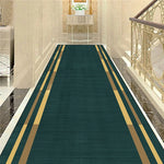 Un long tapis vert avec des bandes dorées, dans un hall d'entrée élégant avec des murs de pierre et une rambarde en métal forgé.