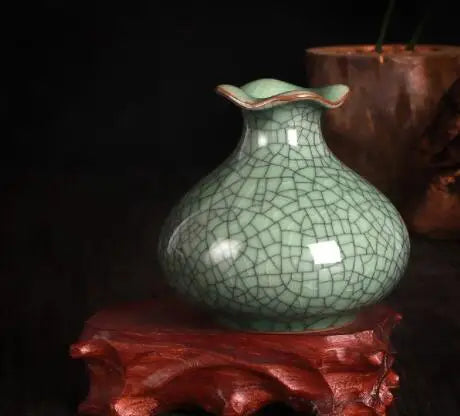 Un vase de céramique vert aux motifs craquelés, posé sur une surface rouge, évoquant une atmosphère chaleureuse et rustique.