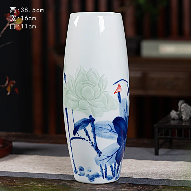 Vase en céramique blanc avec des motifs floraux et aquatiques peints en bleu et vert, placé sur une table en bois dans un intérieur sombre.