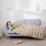 Une femme dormant confortablement sur un canapé gris avec une couverture en duvet beige.