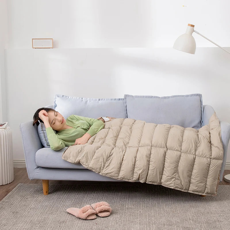 Une femme dormant confortablement sur un canapé gris avec une couverture en duvet beige.