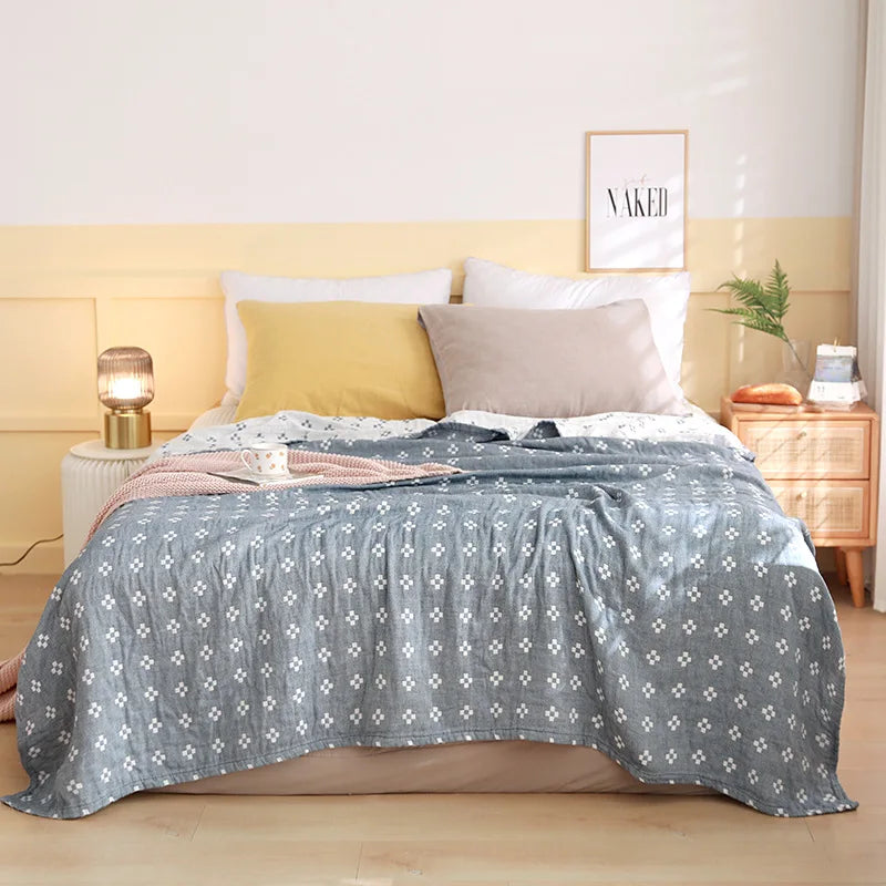 Une chambre à coucher confortable avec des tons pastel, un lit douillet orné d'une couverture motif fleuri grise et blanche, et des accessoires décoratifs élégants.