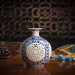 Vase en porcelaine bleu et blanc aux motifs ornementaux élégants, posé sur une table en bois avec d'autres objets décoratifs, créant une atmosphère chaleureuse et raffinée.