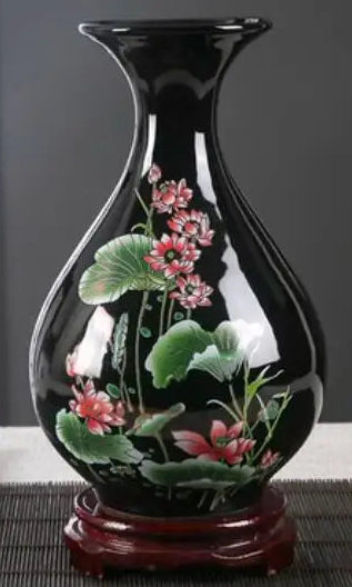Un vase en verre noir décoré de fleurs de lotus roses et de feuilles vertes, posé sur un support en bois.