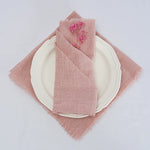 Une nappe en tissu rose pale avec une décoration florale, posée sur une assiette blanche.