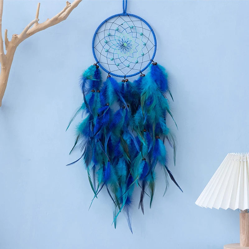 Un attrape-rêves bleu et vert avec un motif spiralé, orné de plumes bleues et vertes, suspendu à un bâton en bois sur un mur.
