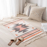 Tapis et coussins décoratifs de style ethnique boho, avec des motifs géométriques et des franges, dans une pièce lumineuse et épurée.
