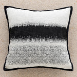 Coussin ornemental avec des motifs abstrait en noir et blanc, créant un contraste visuel élégant sur un tapis beige clair.