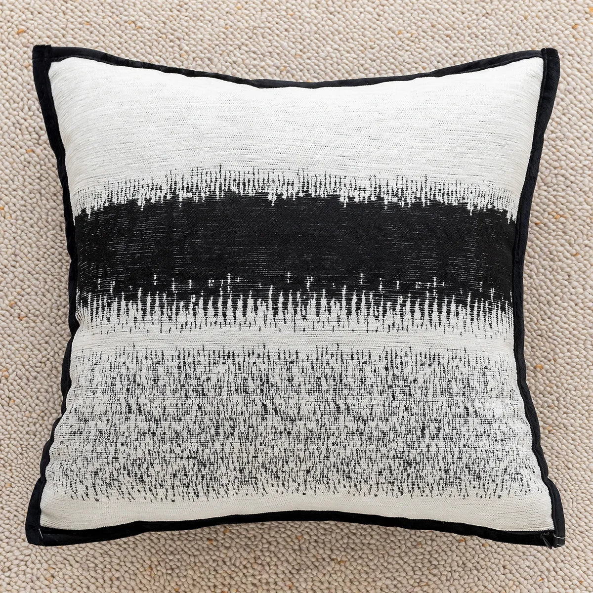 Coussin ornemental avec des motifs abstrait en noir et blanc, créant un contraste visuel élégant sur un tapis beige clair.