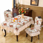 Cette image montre une table à manger élégante avec une nappe ornée de motifs floraux et des chaises assorties, dans un décor de style traditionnel avec un meuble en bois sombre et un cadre mural.