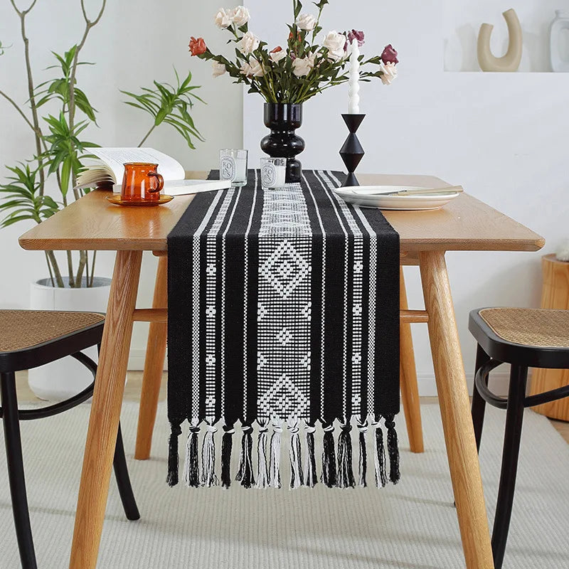 Une élégante table de salle à manger avec un chemin de table décoratif en noir et blanc, des fleurs dans un vase, et des éléments de décoration minimalistes qui apportent une touche de style.